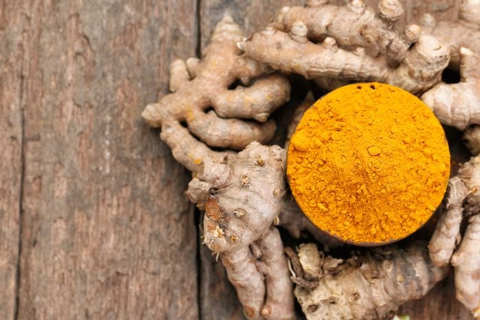 bowl of turmeric powder surrounded by turmeric root