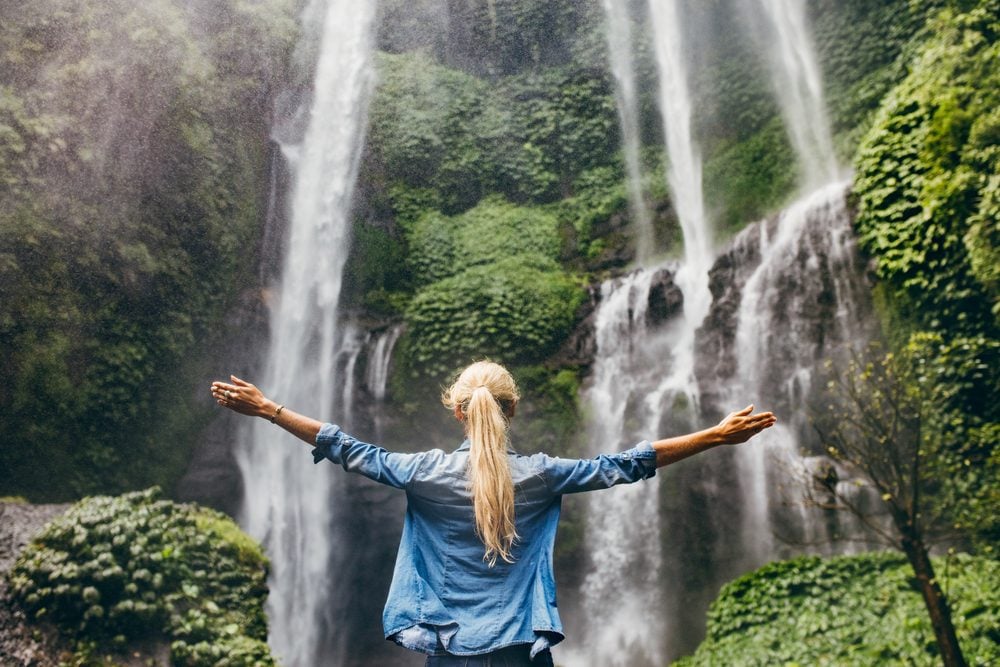 woman standing in front of waterfall with hands up