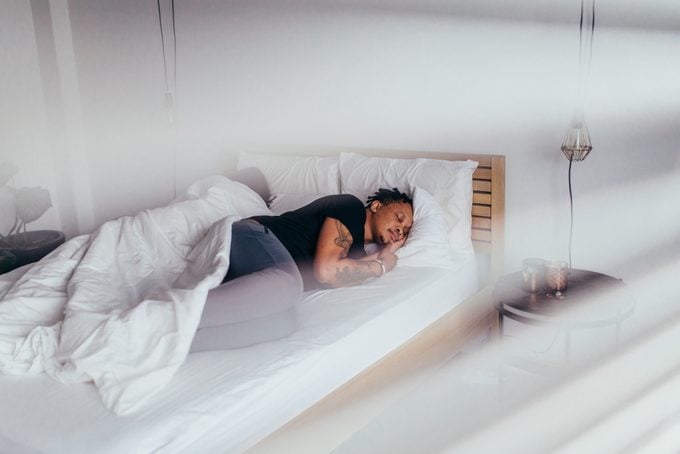 African man sleeping in bedroom with woman at back. Couple sleeping back to back on bed.
