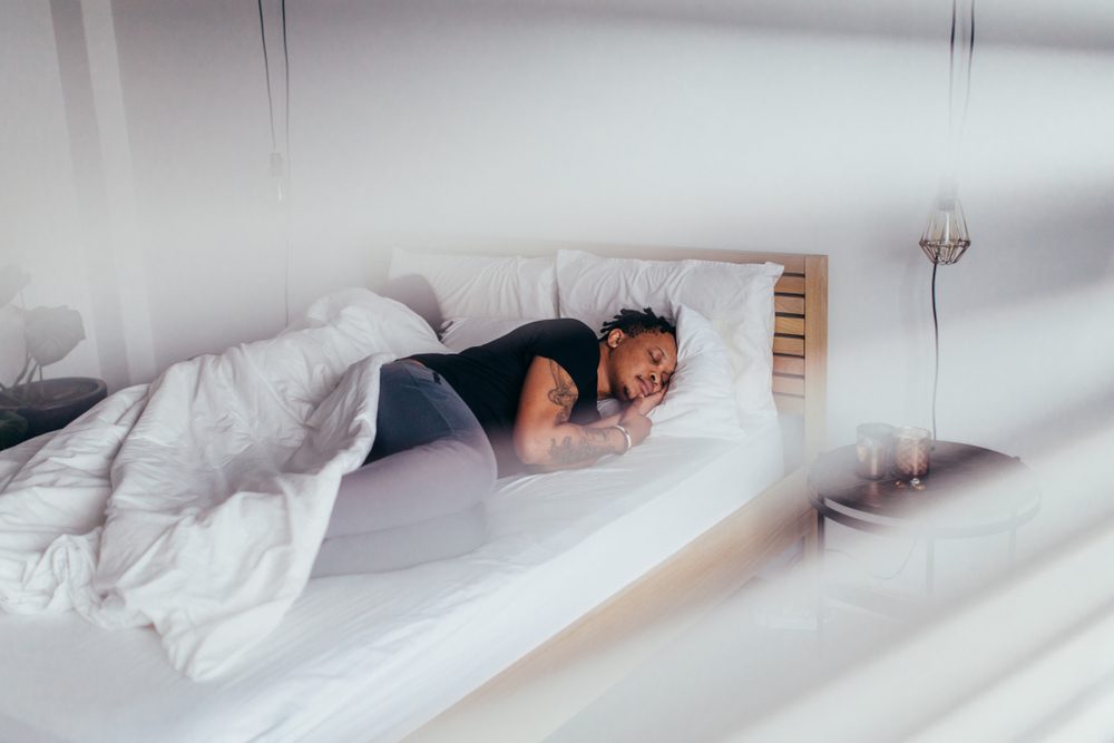 Hombre africano durmiendo en el dormitorio con una mujer detrás. Pareja durmiendo espalda con espalda en la cama.