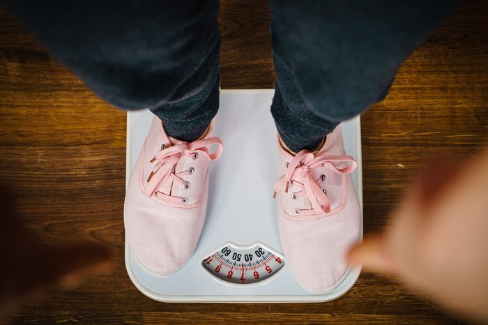 Top view of woman feet wearing pink sneakers on bathroom weight scale. Fit, dieting, fat loss concept.