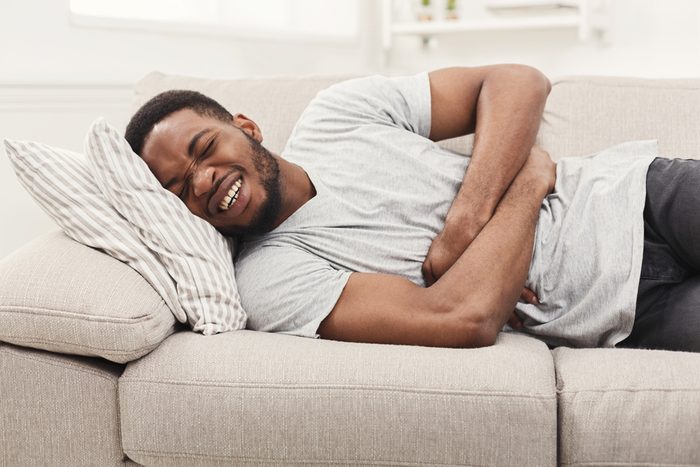 Handsome young african-american man suffering from stomach ache while lying on sofa at home