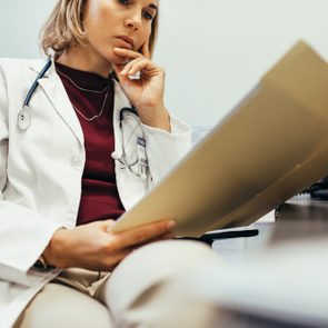 Doctor reading medical documentation in hospital. Female physician sitting in her office and examining medical records.