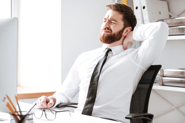 Young businessman sitting in office while stretching.