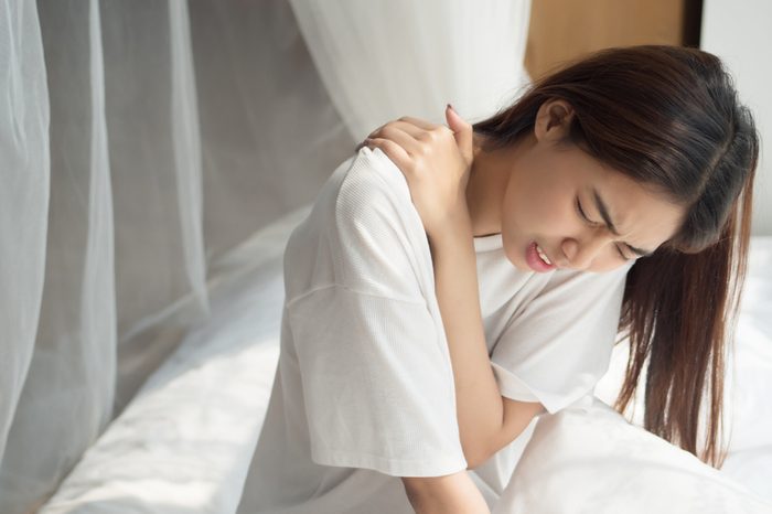 Woman in bed holding her shoulder in pain.