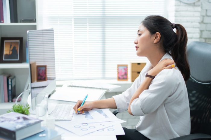Woman at her desk holding her shoulder.