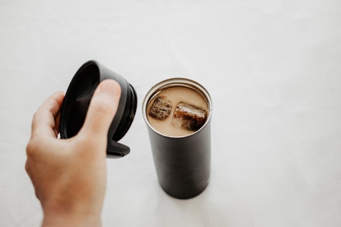 Iced coffee to go. Frozen coffee ice cubes in vacuum flask poured with milk. Hand putting a thermos lid over the bottle. White background, body parts, personal point of view shot. Isolated, copy space