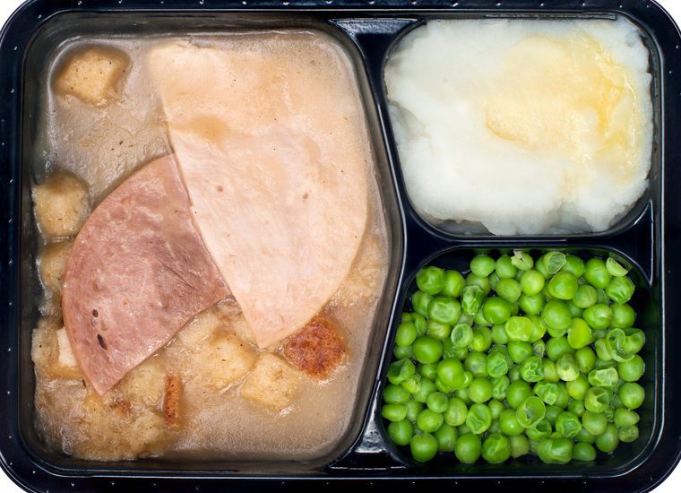 A TV dinner consisting of turkey, ham, peas and mashed potatoes isolated on white