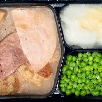 A TV dinner consisting of turkey, ham, peas and mashed potatoes isolated on white