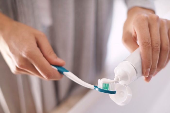 woman putting toothpaste on toothbrush, brushing her teeth