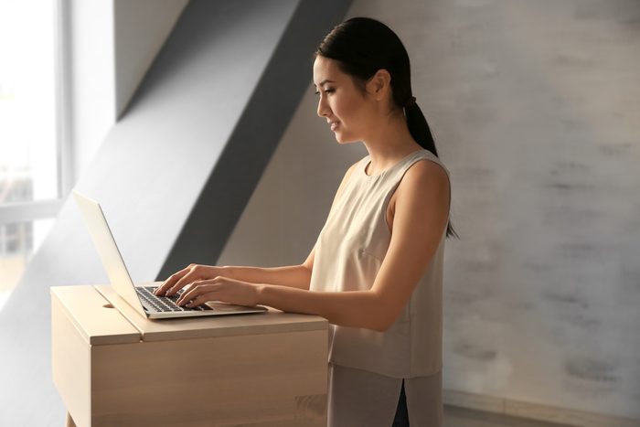 Азиатка печатает на ноутбуке на рабочем месте