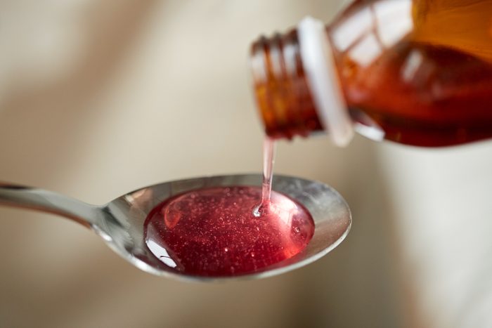 bottle pouring red cough syrup into spoon