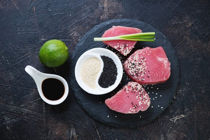 Stone slate tray with raw fresh tuna steaks and condiments, above view on a dark brown stone background, horizontal shot