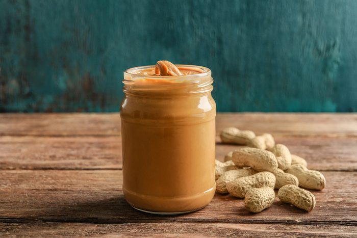 Glass jar with creamy peanut butter on wooden table