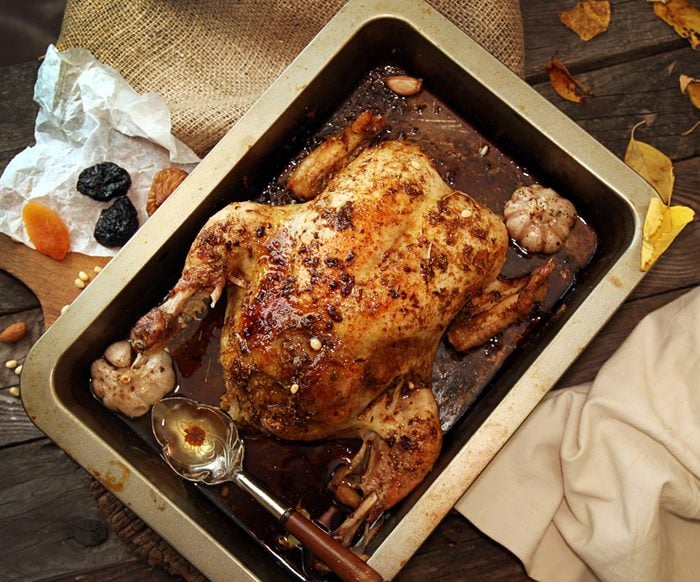 Roasted small turkey for celebration Christmas in roasting pan on old rustic wooden table. Stuffed with couscous with a fig, prunes, dried apricots, almonds and pine nuts