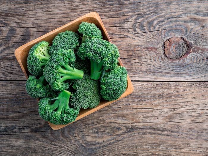 fresh raw green broccoli in wooden bowl on wooden background, top view