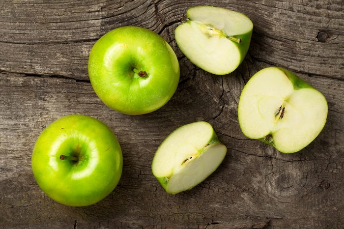 ripe green apples and apple slices on wooden gray background, top view