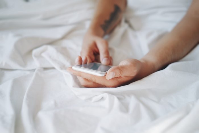 Man's hand holding white mobile smartphone in bed