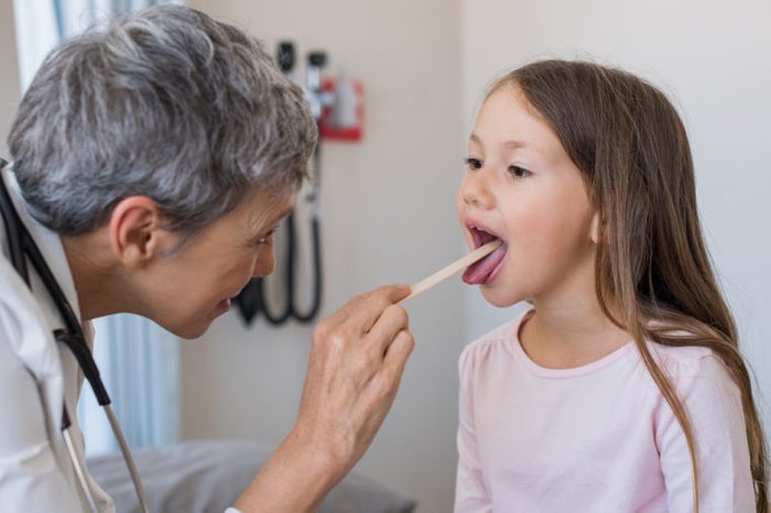 Doctor examining little girl's mouth and tonsils at the doctor's office. 