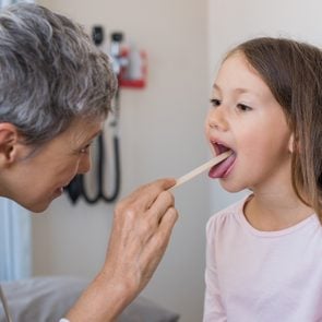 Woman doctor examining little girl mouth at office. Senior doctor at hospital checking the sore throat of a young patient. Pediatrician checking tonsils of a little patient in hospital room.