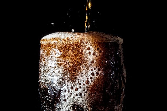 Soda large glass, overflowing glass of soda closeup with bubbles isolated on black background