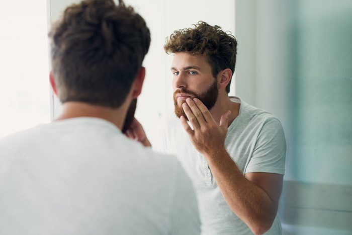 man looking at his beard in the mirror
