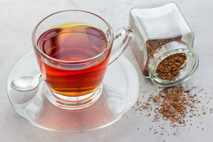 cup of healthy herbal rooibos red tea in glass cup and jar of dry tea
