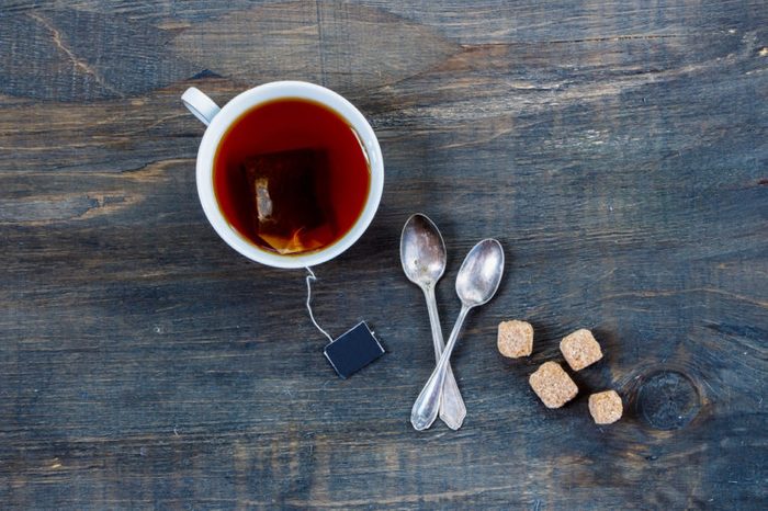 Overhead view of cup of tea with two spoons and cubes of brown sugar