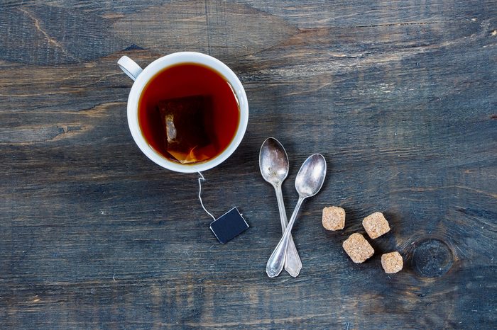 Overhead view of cup of tea with two spoons and cubes of brown sugar