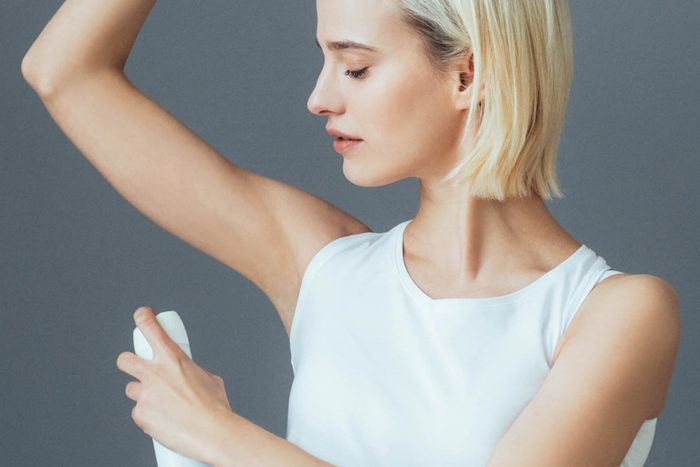 woman applying deodorant spray to armpit