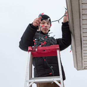 Man hanging Christmas lights during winter from a ladder