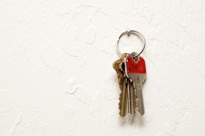 A keyring with three keys hanging on nail on wall.