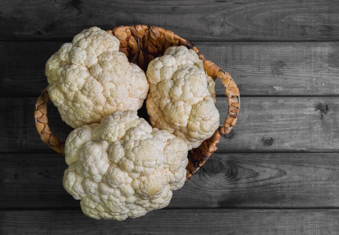 Fresh white heads cleaned cauliflower in a wicker basket for cauliflower. Rustic gray wooden background. Top view, blank space.