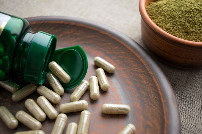 Close up Green capsules, bottle and powder on a clay brown plate on a burlap background. Dietary supplements for Weight Loss and detox. vitamins and minerals for vegans and vegetarians. Superfood