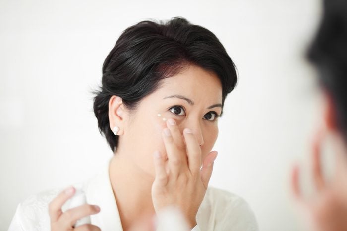 Beautiful female applying facial treatment or cream around her eyes.