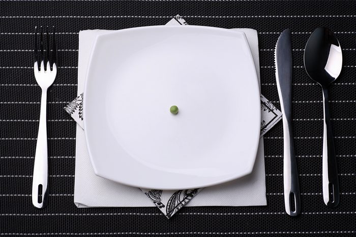 place setting including silverware and white plate filled with One pea
