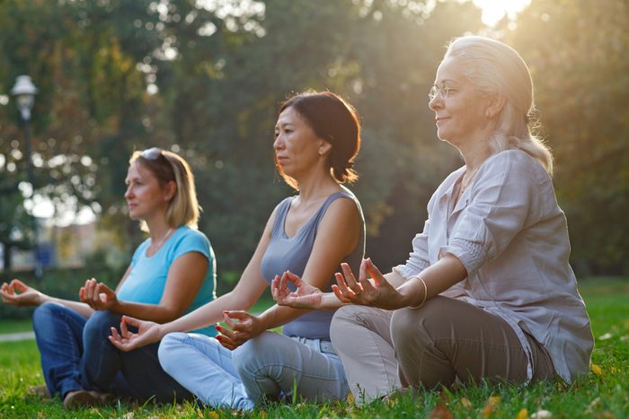 Three ladies meditate while sitting on the grass