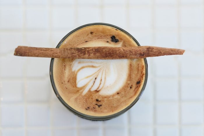 Cup of cappuccino art with cinnamon stick on top over marbel white table background,top view
