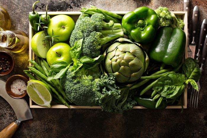 Variety of green vegetables and fruits in a crate on the table