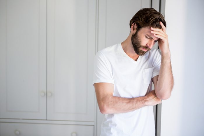 Worried man with hand on forehead leaning on wall at home