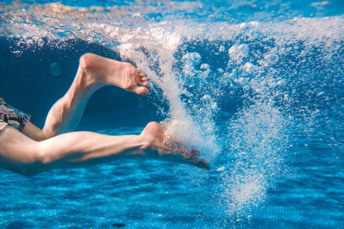 Men's legs swimming underwater in the swimming pool.