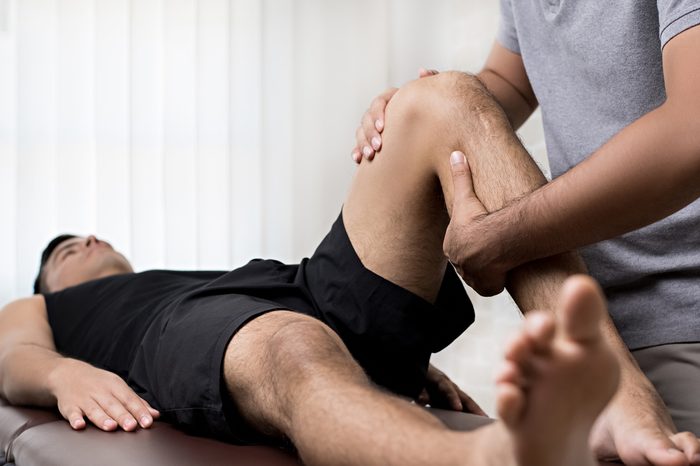 Therapist treating injured knee of athlete male patient.
