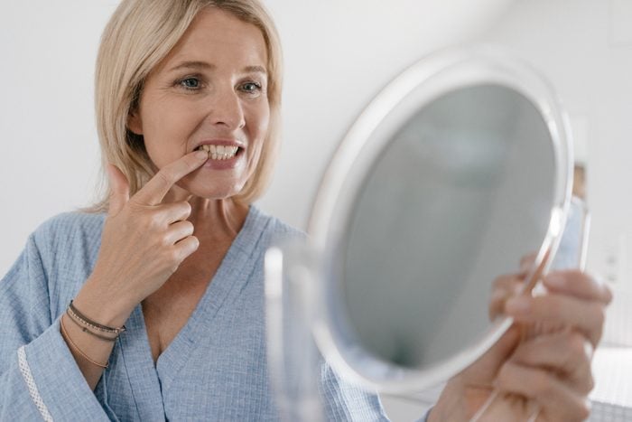 mature woman looking at teeth in handheld mirror