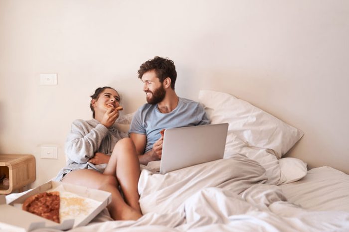 young couple eating pizza in bed