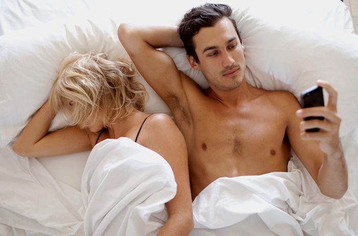 man looking at phone in bed with woman