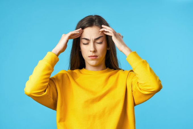 yellow sweater woman headache migraine blue background