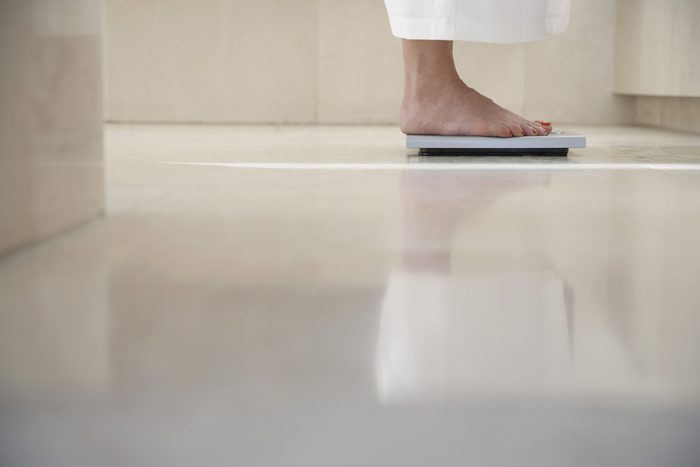 Low section of woman standing on weighing scale in bathroom