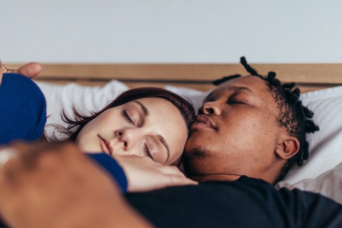 Mixed race couple sleeping together in bed. African man sleeping with caucasian woman at home.
