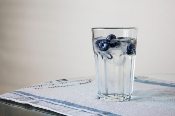 glass of fresh water with blueberry ice cubes on the glass transparent table with blue linen tablecloth