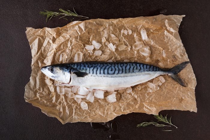 Fresh mackerel fish in ice on craft paper at black background. Organic cooking ingredients for seafood restaurant. Top view, copy space